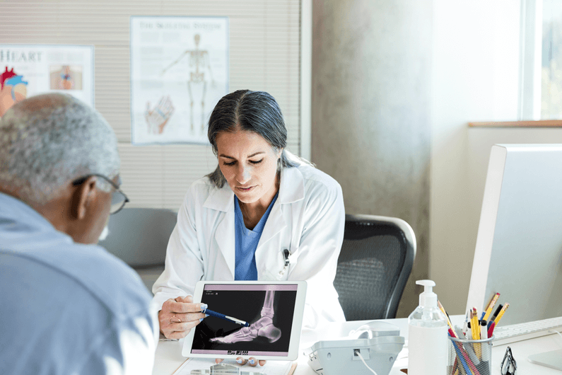 A female doctor uses a tablet to show a male patient an x-ray in her office.