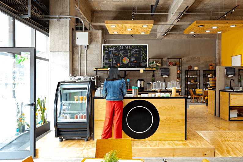 Female customer stands facing the service counter at a local smoothie and juice bar.