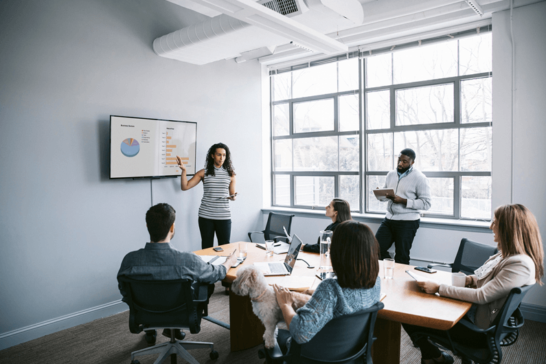 Professionals sit in a bright office and view a presentation on why companies need to accelerate digital transformation.