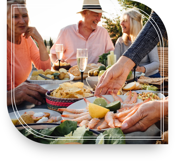 Smiling older man and woman outdoors sitting at a table with food and drink.