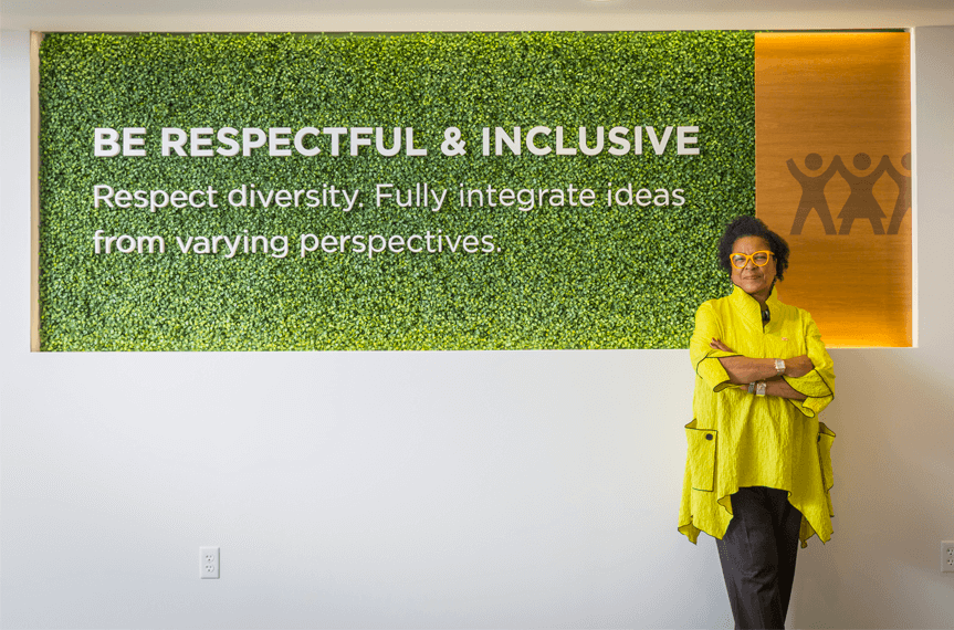 Stephanie Smith standing in front a large sign with the words Be Respectful and Inclusive, Respect Diversity. Fully integrate ideas from varying perspectives.