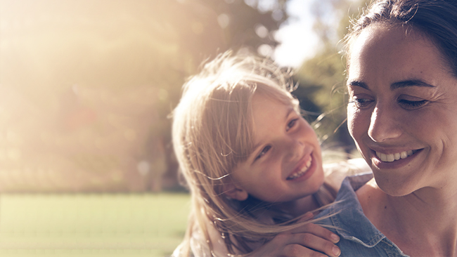 Young blonde girl smiles with golden sunlight shining in the background.