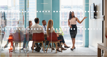 Woman leading a meeting pointing to a screen talking about investment management services.