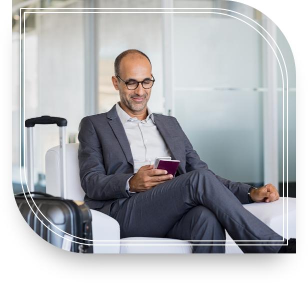 A man with a suitcase sits in a chair looking at his phone, smiling because he is checking his equity compensation. 