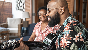 A man sitting on a couch playing a guitar for a woman