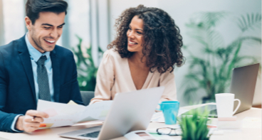 Man and woman looking at papers at a desk talking through investment strategies.