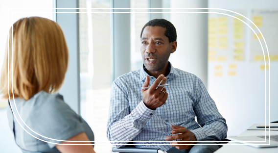 A male retirement advisor holds a pen and discusses high net-worth retirement planning strategies with a female client.