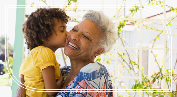 A retired woman smiles as her small granddaughter kisses her on the cheek.