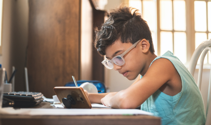 A child sitting at a desk watching a Young Bankers Club financial literacy lesson